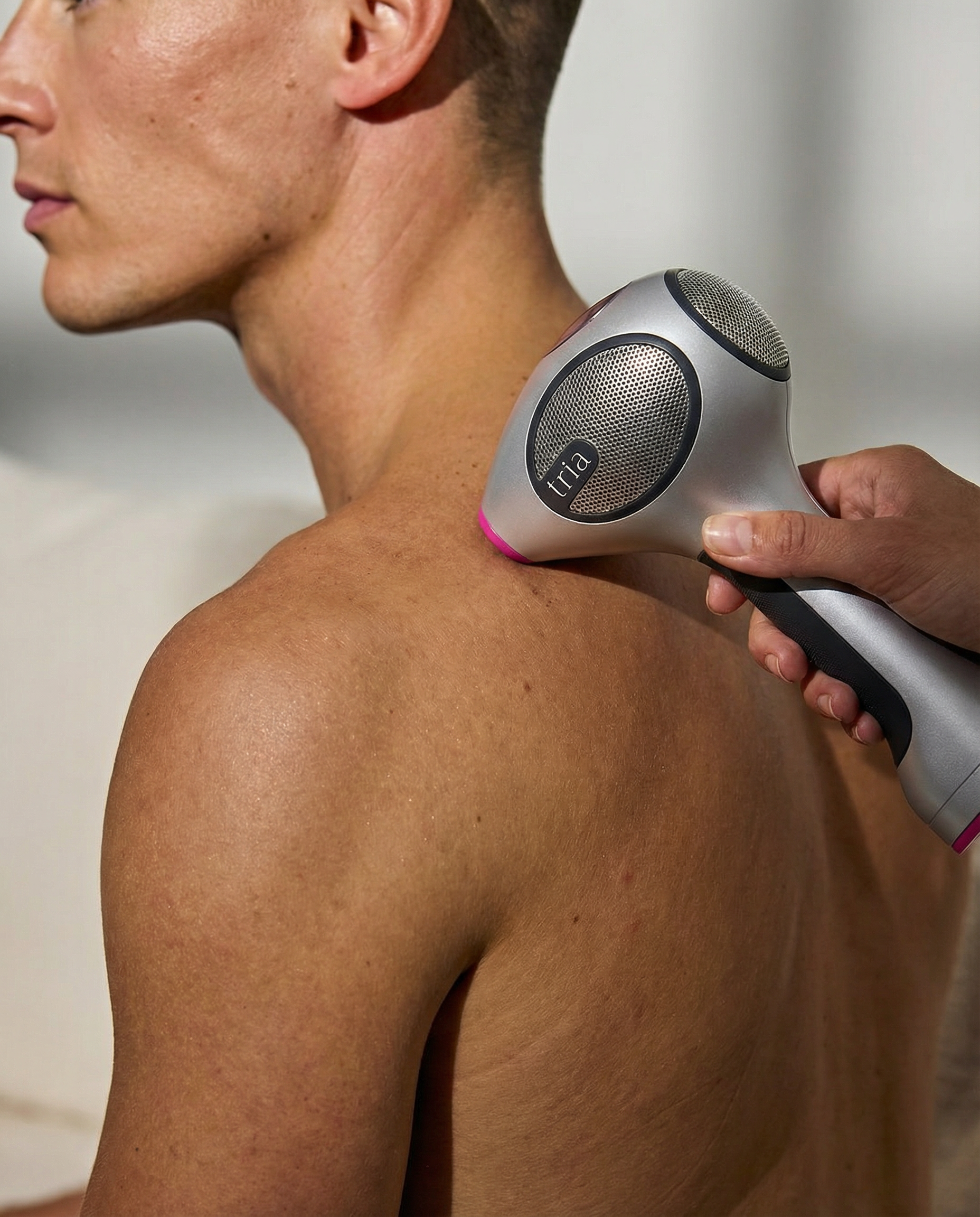 Man using a hair removal device on their back against a neutral background